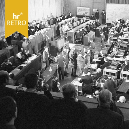 Blick in den Gerichtssaal während des Auschwitz-Prozesses 1963 in Frankfurt am Main. Zu sehen sind Angeklagte, Anwälte, Richter, Zuschauer und Pressevertreter in einer vollen Verhandlungsszene.
