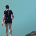 Eine Frau in schwarzer Shorts und schwarzem Shirt von hinten zu sehen, geht Richtung Horizont. Im Hintergrund Berge und Quallen.