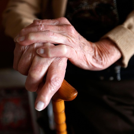 Nahaufnahme der Hände einer Seniorin, die sich an einem Gehstock festhält.