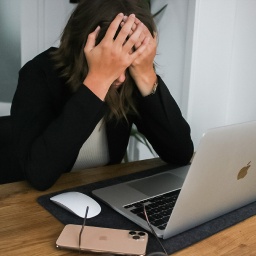 Eine Frau sitzt vor ihrem Laptop und vergräbt verzweifelt das Gesicht in ihren Händen