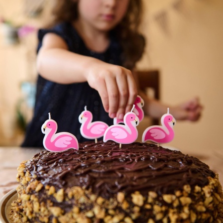 Ein Mädchen dekoriert eine Torte mit Flamingokerzen