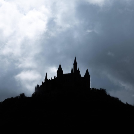Die dunkle Silhouette einer Burg ist vor einer Wolkendecke zu sehen. 
