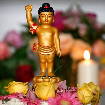 Buddhistisches Vesak-Fest: Eine kleine goldene Figur steht inmitten von Blumen, im Hintergrund brennt eine Kerze.