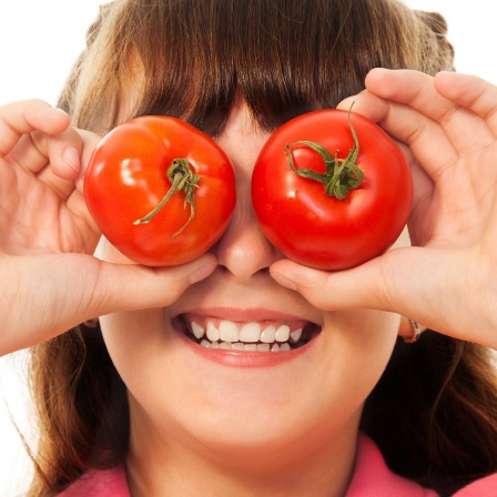 Lachendes Kind hält sich 2 Tomaten vor die Augen.