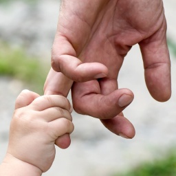 Ein Kind hält sich an der Hand des Vaters fest.