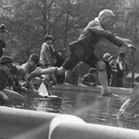 Eine Gruppe von Kindern spielt 1930 an einem Brunnen, schwarz-weiß Bild.