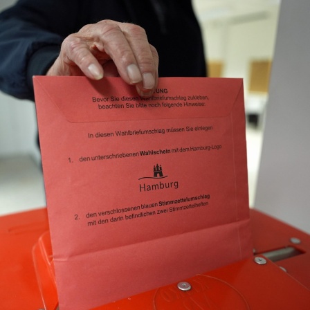 Ein Wähler steckt die Stimmzettel nach seiner Wahlabgabe in eine Wahlurne in der zentralen Briefwahlstelle zur Bürgerschaftswahl und Bundestagswahl 2025 auf dem Gerhart-Hauptmann-Platz.