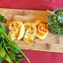 drei Blätterteigschnecken mit verschiedenem Frischkäse auf einem Holzbrett, daneben ein Glas mit Rucola-Frischkäsekugeln und ein Bündel Kräuter