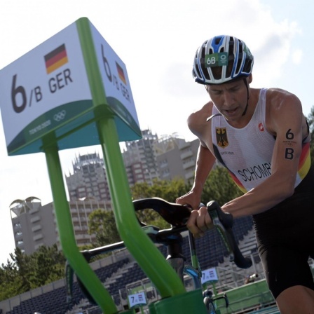 Der deutsche Triathlet Jonas Schomburg nimmt bei den Olympischen Spielen in Tokio in der Wechselzone sein Rennrad in Empfang. 