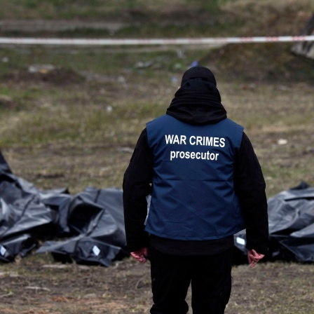 Ein Ermittler eines internationalen Forensik-Teams trägt eine Weste mit der Aufschrift «War Crimes Prosecutor» («Ankläger für Kriegsverbrechen») und beginnt damit, neben Leichen aus einem Massengrab hinter der Kirche St. Andreas Beweise für Kriegsverbrechen zu sammeln.
