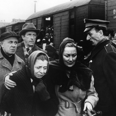 Filmszene Fernsehserie &#034;Holocaust&#034;: Zwei Frauen in einer Menschenmenge halten sich im Arm, im Hintergrund ein Güterzug mit Menschen gefüllt