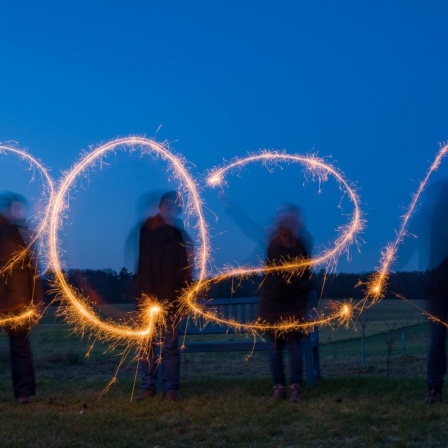 Vier Personen stehen auf einem Feld und schreiben mit Wunderkerzen die Jahreszahl "2021" in den Abendhimmel (Langzeitbelichtung, gestellte Aufnahme).