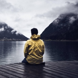 Ein Mann in einer gelben Jacke sitzt auf einem Holzsteg und blickt auf einen Bergsee