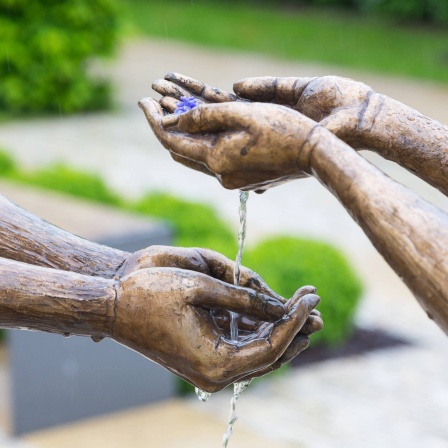 Hände zweier Bronzefiguren, die sich Wasser reichen: Im Mittelalter hat man mit den Fingern gegessen. Zur Reinigung der Hände wurden Wasserschalen gereicht. Allerdings geschah das nicht auf Augenhöhe. Von diesem Brauch leitet sich die Redensart ab: Jemandem nicht das Wasser reichen können
