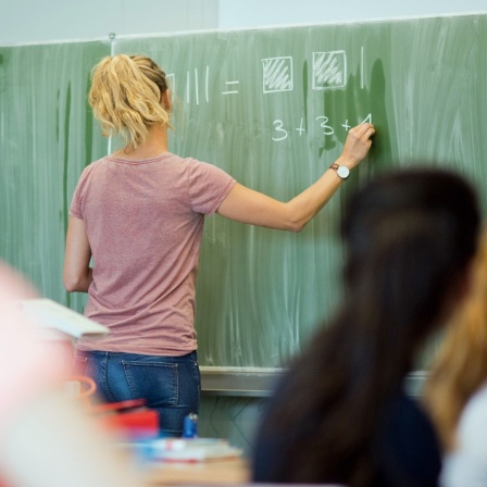 Eine junge Lehrerin schreibt an einer Schultafel.