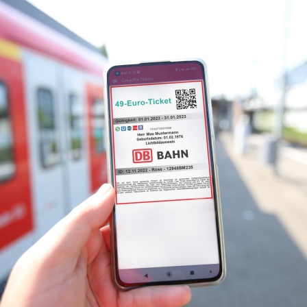 Hand hält Smartphone auf dem ein Bahnticket mit der Überschrift "49-Euro-Ticket" zu sehen ist