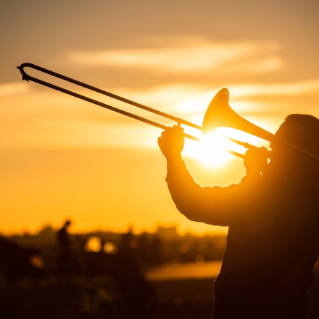Ein Mann spielt während des Sonnenuntergangs auf dem Tempelhofer Feld Posaune.