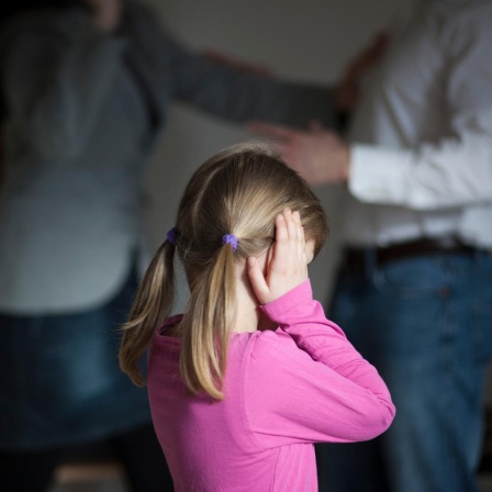 Zwei Erwachsene streiten sich, während die Tochter dazwischen steht und sich die Ohren zuhält. 