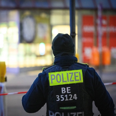 Ein Polizist steht an einem Tatort vor einem Absperrband.