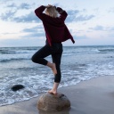 Eine Frau balanciert auf einem Stein am Meer.