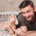 Ein Mann kitzelt die Füße einer anderen Person
