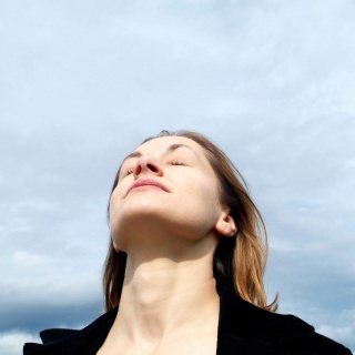 Das Beitragsbild des WDR 3 Kulturfeature "Atmen, du unsichtbares Gedicht" zeigt eine Frau vor blauem bewölkten Himmel die tief Luft einatmet. 