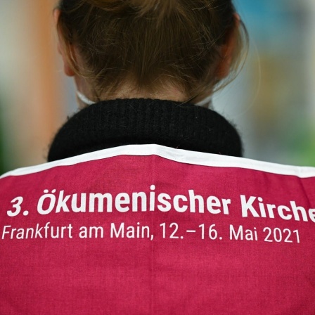 Eine Mitarbeiterin des Ökumenischen Kirchentags präsentiert ein ÖKT-Tuch mit der Aufschrift "3. Ökumenischer Kirchentag Frankfurt am Main, 12. - 16. Mai 2021.