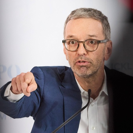 Herbert Kickl spricht auf einer Pressekonferenz und deutet mit seiner rechten Hand nach vorne.