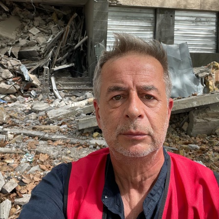 Andreas Tölke macht ein Selbstportrait vor einem zerstörten Haus in der Ukraine