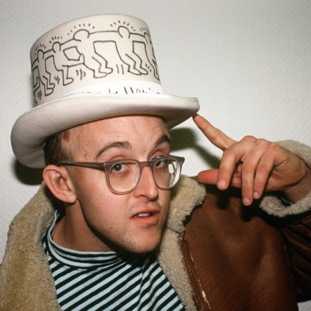 Der US-amerikanische Graffiti-Künstler Keith Haring posiert 1990 mit einem Zylinder-Hut, auf dem seine berühmten "Männchen" abgebildet sind.