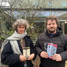 Lisa Kreißler und Alexander Solloch stehen mit Büchern in der Hand auf einem Innenhof und schauen in die Kamera.