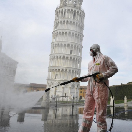 Ein Arbeiter in kompletter Schutzkleidung führt am 17. März 2020 in Pisa auf der Piazza dei Miracoli  sanitäre Maßnahmen für den Coronavirus-Notfall durch. Im Hintergrund ist der bekannte schiefe Turm von Pisa zu sehen.