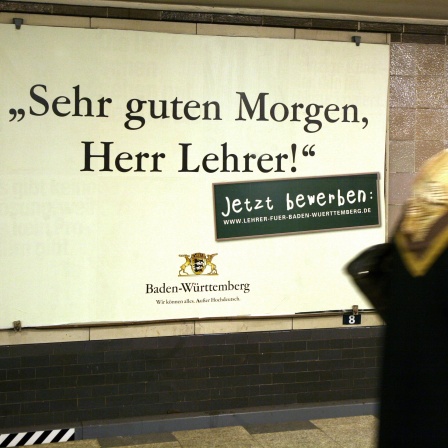 Eine Frau läuft in einem Berliner U-Bahnhof an einem Werbeplakat vorbei, auf dem Baden-Württemberg für den Lehrerberuf wirbt. Darauf steht in einer altmodischen Schrift der Satz: "Sehr guten Morgen, Herr Lehrer." 