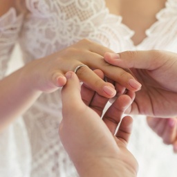 Ein Bräutigam steckt seiner Braut den Ehering an den Ringfinger.