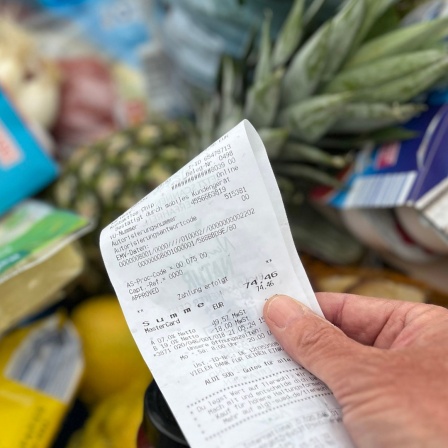Ein Supermarkt-Kunde überprüft seinen Kassenbon von einem gut gefüllten Einkaufswagen