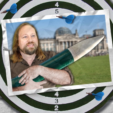 Eine Bildmontage zeigt eine Dartscheibe. Darauf ist eine Postkarte mit einer Fotomontage zu sehen, die Anton Hofreiter von den Grünen mit einer Rakete im Arm zeigt. 