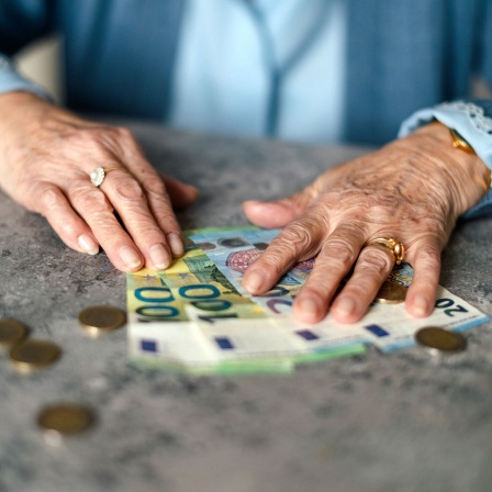Seniorin zählt Geldscheine und Münzen auf einem Tisch.