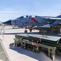 Im Vordergrund ein grüner Taurus-Marschflugkörper, im Hintergrund ein graues Kampfflugzeug der Bundeswehr