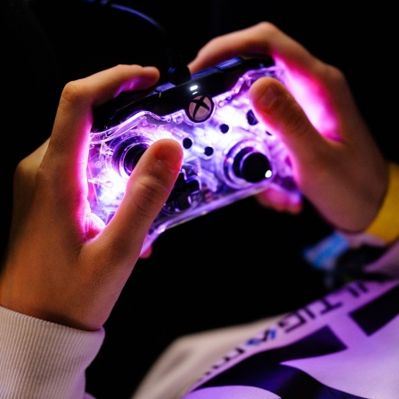 Eine leuchtender X-Box-Controller zwischen zwei Händen