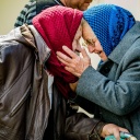 Zwei alte Frauen mit Kopftuch umarmen sich. 