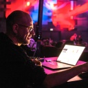 Der Medienkünstler Robert Henke schaut konzentriert auf einen Laptop und dreht an Reglern, der ganze Raum ist in rotes und blaues Licht getaucht.