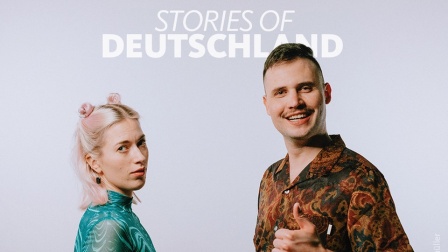 Die Hosts des Podcasts "Stories of Deutschland" Sina und Marius schütteln sich die Hände. Marius zeigt einen Daumen nach oben.