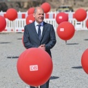 Bundeskanzler Olaf Scholz (SPD) steht zum symbolischen Spatenstich für ein neues Bahnwerk zwischen roten Luftballons mit dem Deutsche Bahn (DB) Logo. 
