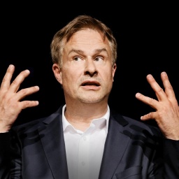 Lars Reichow vor schwarzem Hintergrund, streckt alle zehn Finger in die Höhe und schaut zur Seite