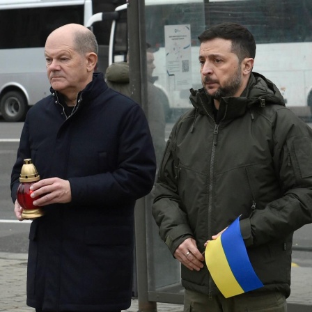 Olaf Scholz und Wolodymyr Selenskyj beim Gedenken an Kriegstote auf dem Majdan Nesaleschnosti in Kiew, die Politiker halten eine Kerze und eine Ukraine-Flagge.