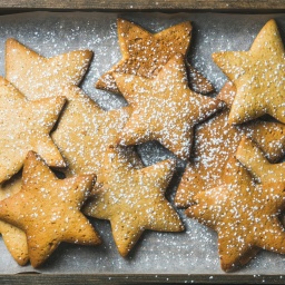 Süße weihnachtliche Lebkuchenplätzchen in Form von Sternen mit Puderzucker auf Backpapier