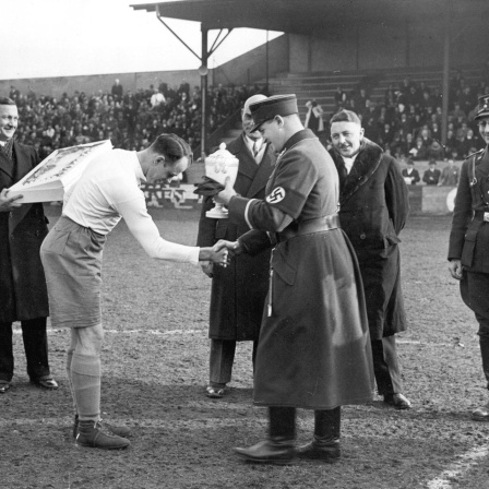 Hanne Sobek von Hertha BSC (links) erhält den Meisterschaftspokal in der Gauliga durch Gauführer Glöckler im März 1935 (vorn rechts) ca. März 1935 in Berlin. Gauliga Berlin-Brandenburg. 