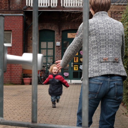 Ein kleines Kind läuft in die geöffneten Arme seiner Mutter, währens die es vom Kindergarten abholt.