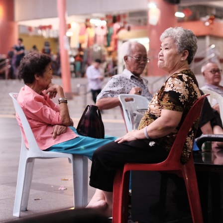 Senioren sitzen auf Plastikstühlen am Eingang eines Tempels in Chinatown, Singapur