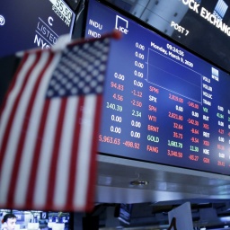 Ein Bildschirm zeigt Amerikanische Aktienkurse, im Vordergrund ist eine Amerikanische Flagge zu sehen. Aufnahme vom 09.03.2020